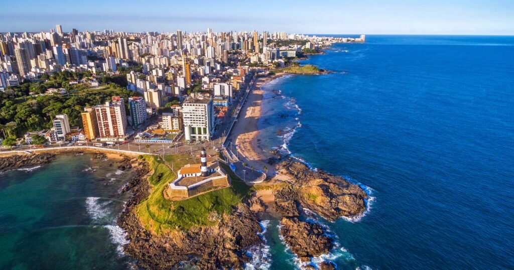 該圖片展示了巴西薩爾瓦多的海岸線,明亮的藍色海洋與現代城市建築相映成趣。畫面中可以看到歷史悠久的燈塔矗立於海岸,周圍的海灘吸引著眾多遊客,完美呈現了都市與自然的和諧結合。